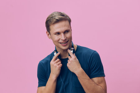 Smiling man with headphones, casual blue t-shirt, happy expression, young adult, isolated on pink...