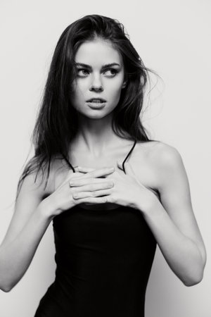 Pensive young woman with long hair posing in a black top, hands clasped in front, against a minimalist gray background. Concept of contemplation and self-reflection.の写真素材