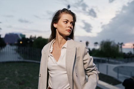 Woman in beige business suit looking away with contemplative expression in outdoor urban environment during sunset with soft natural lighting and light blue skyの写真素材
