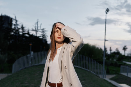 Confident businesswoman in a stylish outfit, standing outdoors against a sunset backdrop, conveying...