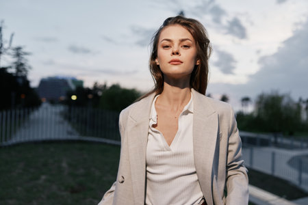 Businesswoman in a light blazer exuding confidence in an urban setting, capturing a modern professional vibe with a soft color palette at dusk.の写真素材