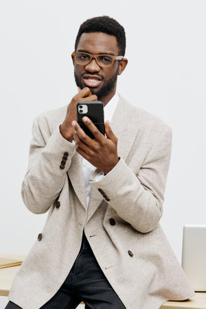 Confident man using smartphone with glasses and curly hair, wearing a beige sweater, in modern office setting. Male technology lifestyle concept, professional, casual attire, indoors, neutral background.の写真素材
