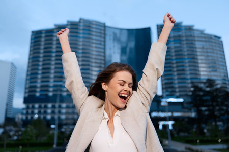 Excited woman celebrating financial success outdoors in modern urban business district, confident...