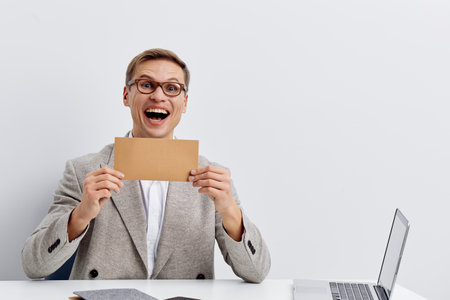 cheerful man holding envelope surprised expression sitting at laptop digital nomad remote work conceptの写真素材