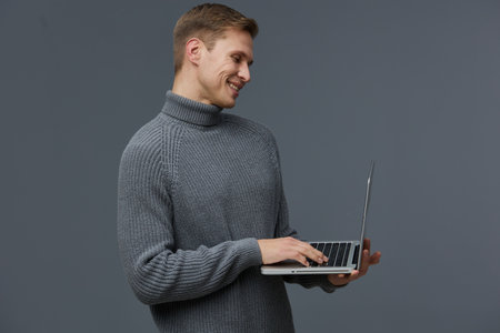 smiling man working with laptop wearing gray turtleneck sweater on dark studio background digital nomad conceptの写真素材