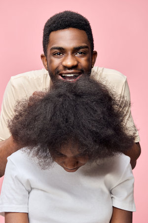 Happy young couple with natural hair against a pink background, showcasing hairstyles and joyful emotions, perfect for hair care concepts and diversity representationの写真素材