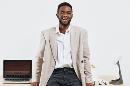 Confident smiling man of African descent with dark skin, wearing beige blazer and white shirt,...