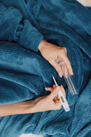 Person laying on bed with blue blanket holding bottle of nail polishの写真素材