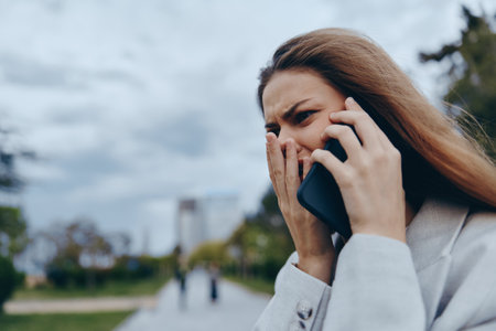 Businesswoman with a phone showing emotion in a city park setting, reflecting modern professionalism and urban lifestyle.の写真素材