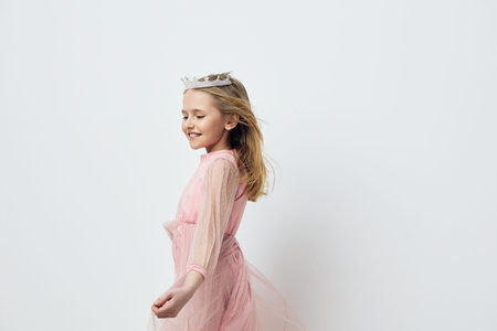 Joyful girl in a pink tulle dress with a crown, dancing happily against a minimalist white background, capturing a carefree and playful momentの写真素材