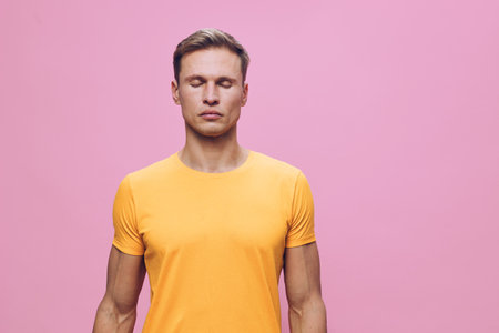 young man meditating with closed eyes wear orange t-shirt isolated on pink background wellness mental health concept mindfulness relaxation calmnessの写真素材