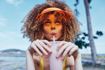 Young woman enjoying a smoothie outdoors with a vibrant backgroundの写真素材