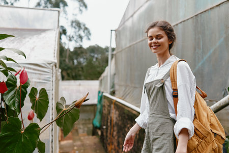 Smiling young woman in stylish overalls exploring a greenhouse, surrounded by vibrant plants,...