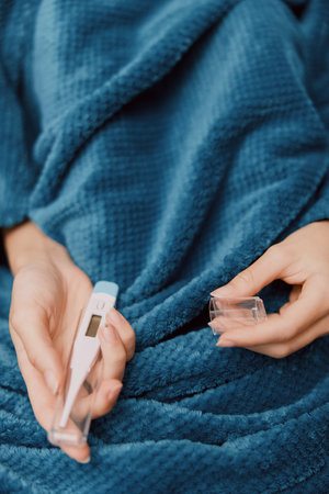 Woman holding thermometer wrapped in blue blanket with another thermometer on bed