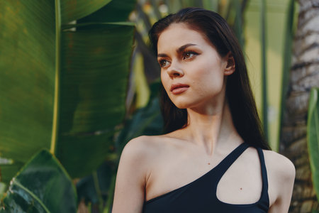 Stylish woman in black oneshoulder top posing in front of lush palm trees on sunny day