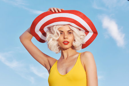 Stylish woman wearing a red and white striped hat with wavy blonde hair against a bright blue sky...