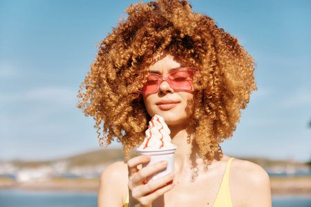 Young woman with curly hair enjoying ice cream on a sunny day by the seaの写真素材
