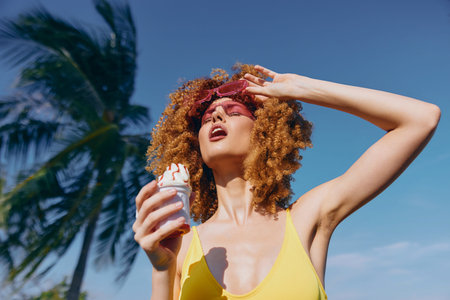 Young woman with curly hair enjoying ice cream under the sunの写真素材