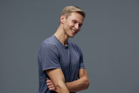 Smiling man with casual blue t-shirt standing against plain grey background studio portrait. Happy, cheerful, relaxed, young adult, male, leisure, positive vibe.の写真素材