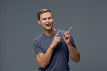 Smiling man pointing fingers gesture look copy space wear casual blue t-shirt isolated grey background studio portrait digital detox tech conceptの写真素材