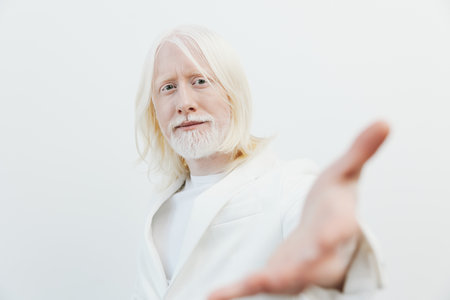 elderly man with long white hair and beard, wearing a white outfit, reaching out with his hand against a light background, conveying openness and warmth in a minimalist settingの写真素材