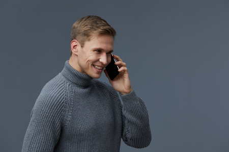 smiling man talking phone wearing gray knitted sweater looking aside communication concept