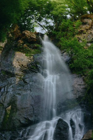 Waterfall flowing down rocky cliffs surrounded by lush green forest foliage under natural daylight...