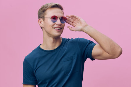 smiling man wear sunglasses hold mobile phone look away positive emotion blue tshirt pink background...