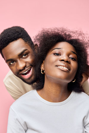 Happy young couple with natural hair, smiling on a pink background, showcasing love and joy in a playful and intimate momentの写真素材