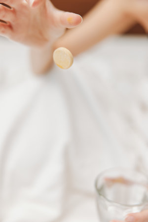 Person sitting on bed with glass of water and food on table in front of themの写真素材