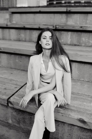 Confident woman in business attire sitting on wooden stairs, exuding elegance and professionalism in a monochrome setting.の写真素材