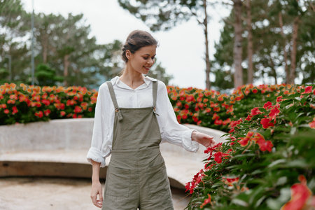 Young woman in casual attire enjoying flowers in a vibrant garden, expressing joy and serenity, perfect for seasonal and lifestyle themesの写真素材