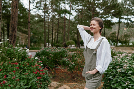 Young woman in casual outfit smiling in a blooming garden, surrounded by vibrant flowers and greenery, embodying joy and nature in springtimeの写真素材