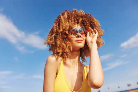Young woman with curly hair wearing sunglasses on a sunny beach backgroundの写真素材