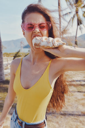 Young woman enjoying a snack outdoors in a sunny tropical setting with palm trees