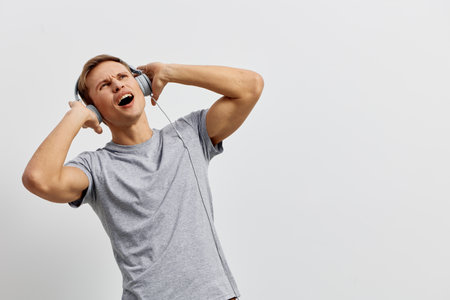Young caucasian man joyful casual wear gray t-shirt listen music with wired headphones isolated on...