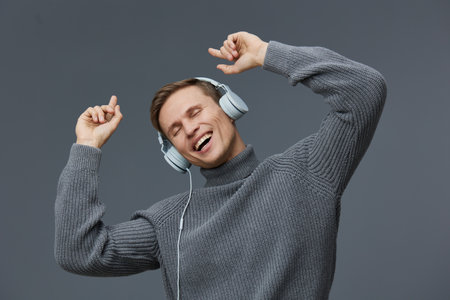 happy young man listen music wear grey knitted sweater headphones enjoy sound with closed eyes...