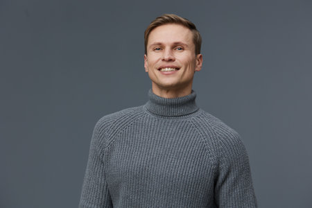 Confident smiling man with short hair wearing gray turtleneck sweater looking at camera isolated on plain gray background studio portrait. People lifestyle conceptの写真素材