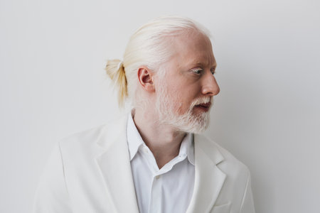 Portrait of a bearded man with long white hair in profile, set against a minimalist white...