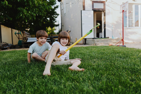 Two cheerful children enjoying a sunny day in the backyard, laughing and playing with a colorful water toy on the green grass, capturing the joy of childhood.の写真素材