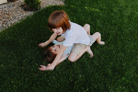 Two children playing happily outdoors on green grass, enjoying a sunny day in a playful atmosphere, expressing joy and innocence in their carefree moment.の写真素材