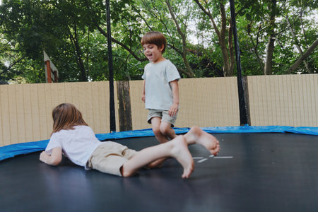 Joyful children playing on a trampoline, enjoying their summer day outdoors in a lively, green backyard setting.の写真素材