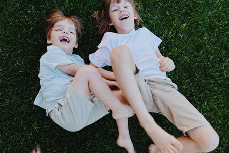 Happy children playing on grass, enjoying a sunny day with laughter and joy. Their playful spirit embodies the essence of carefree childhood moments.の写真素材