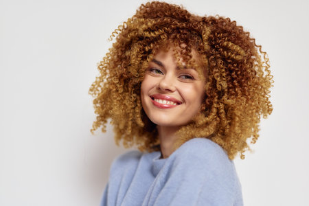 Smiling woman with curly hair against a light background, showcasing vibrant natural curls and a...