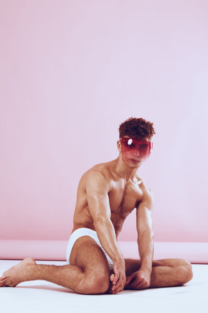 Stylish young man posing in pink background, wearing sunglasses and minimalist white underwear. Fashion and self-expression concept.の写真素材
