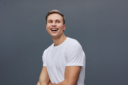 Smiling happy young man wearing white t-shirt look camera isolated on plain gray background studio...