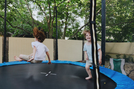 Joyful children playing on a trampoline, showcasing excitement and laughter in a vibrant outdoor setting, surrounded by greenery and sunshine.の写真素材