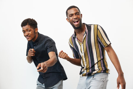 Two cheerful African American men are dancing, showcasing their joy and enthusiasm. The vibrant colors of their shirts brighten the playful atmosphere, ideal for a lively scene.の写真素材