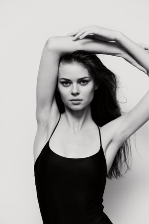 Elegant young woman showcasing confidence with arms raised, wearing a black bodysuit. Bold black and white portrait emphasizing beauty and strength.の写真素材