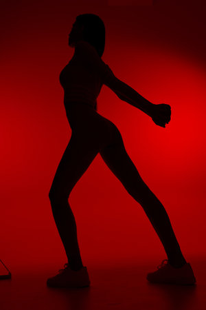 Silhouette of a woman sport fitness stretching her arms and legs against a vibrant red background, showcasing strength, balance, and flexibility for active lifestyle.の写真素材